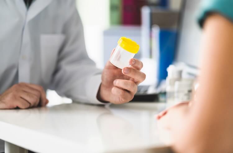 A lab technician hands a urine sample cup to a patient for a uranalysis