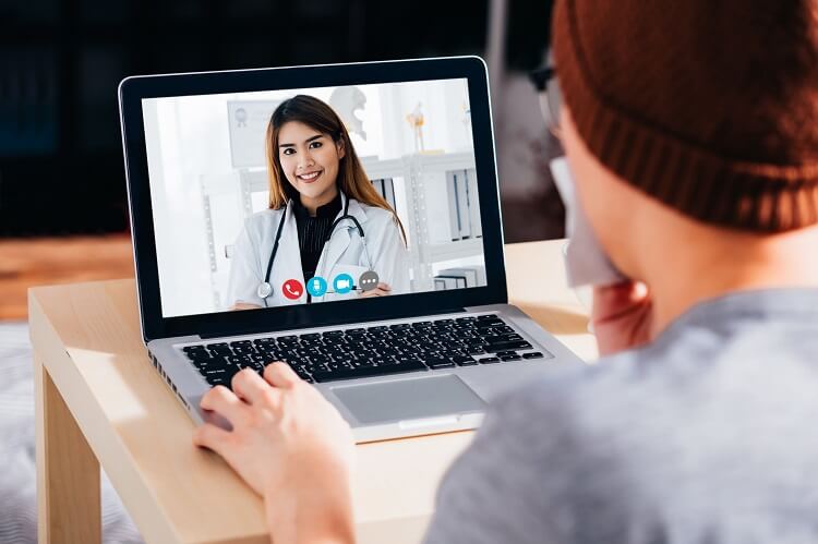 A man visits with a doctor online while holding a handkerchief to his mouth